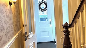 Käytävä, jossa on valkoinen ovi, musta seppele ja seinälle asennettu valaisin.