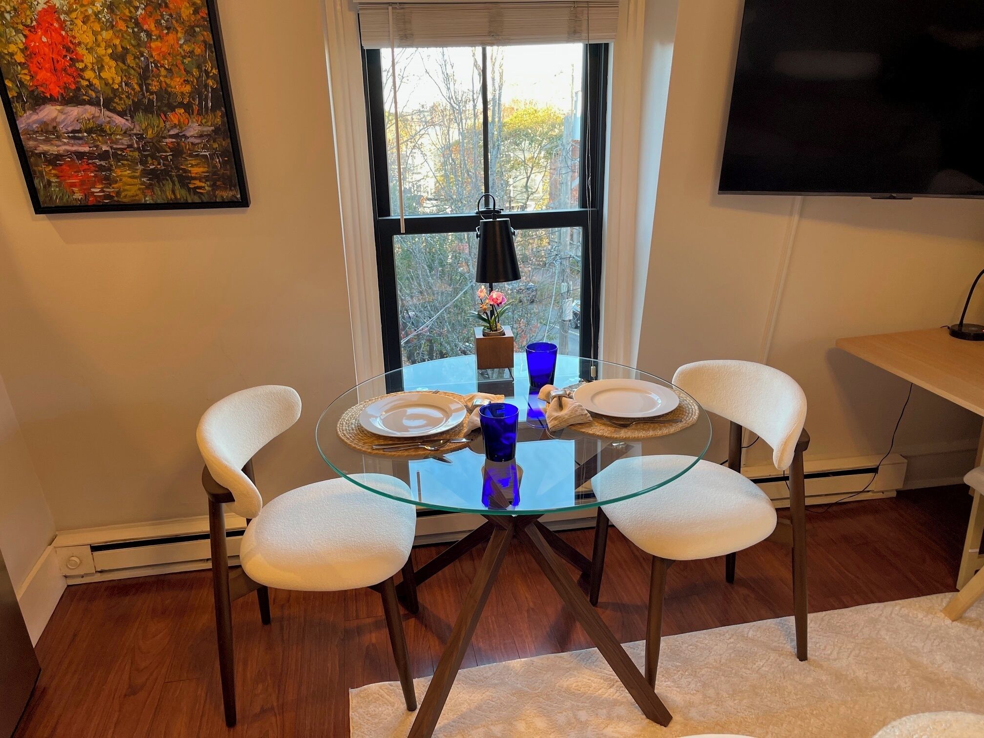 Un coin repas avec une table en verre, des chaises blanches rembourrées et un tableau accroché au mur.
