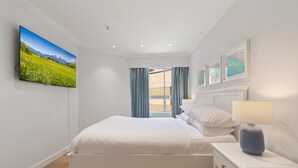 A bedroom with a bed, a nightstand, a lamp, a window with curtains, and a wall-mounted TV displaying a landscape. - Bright & Spacious 1-bed in Vibrant Sydney (Sydney)