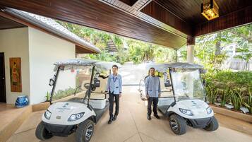 Two golf carts parked under a covered area with a wooden ceiling and potted plants around.