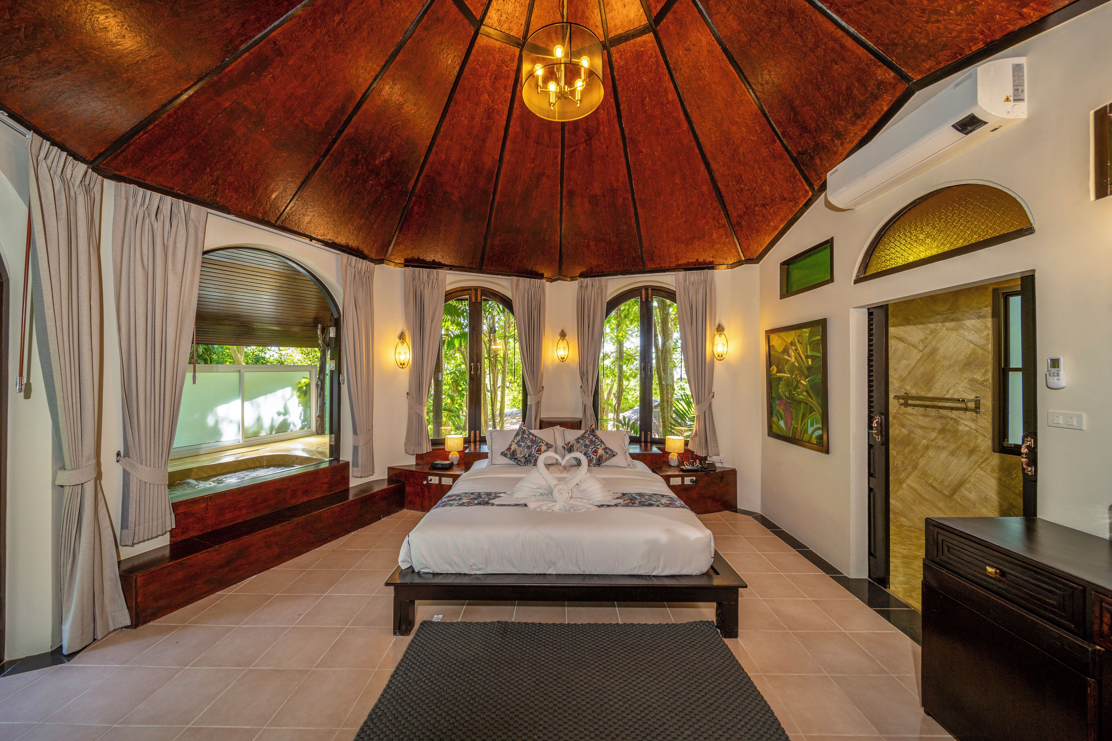 A spacious bedroom with a large bed, multiple windows, and a wooden ceiling.