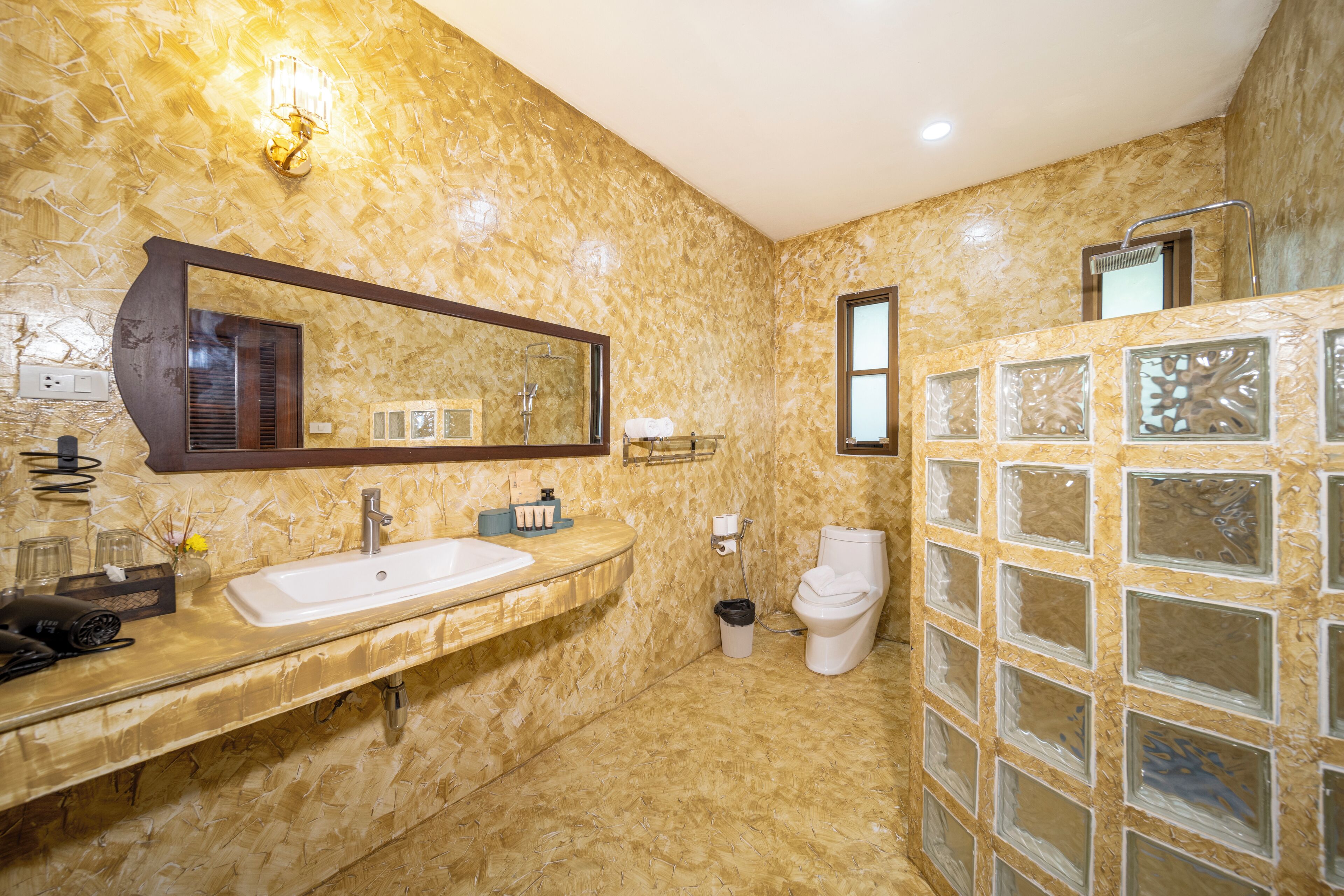 A bathroom with a marble wall, a large mirror, a sink, a toilet, and a glass shower enclosure.
