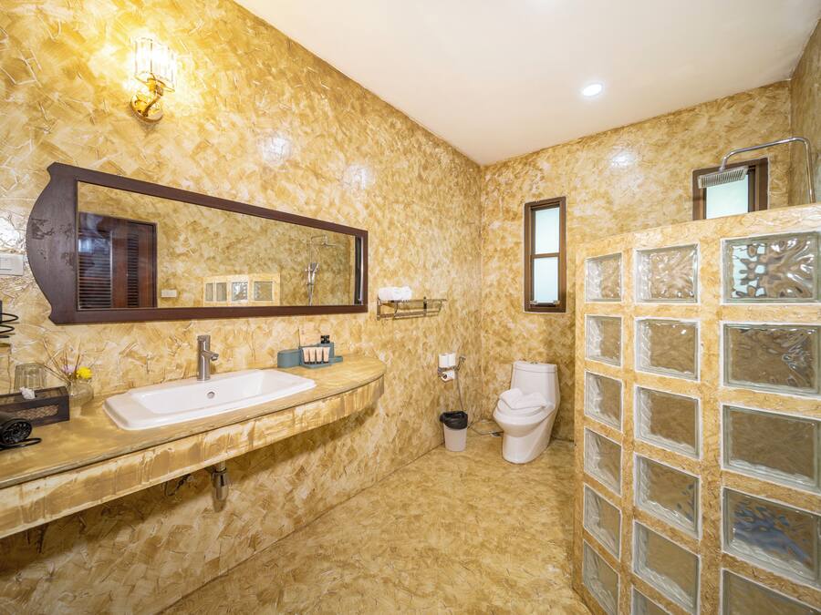 A bathroom with a marble wall, a large mirror, a sink, a toilet, and a glass shower enclosure.
