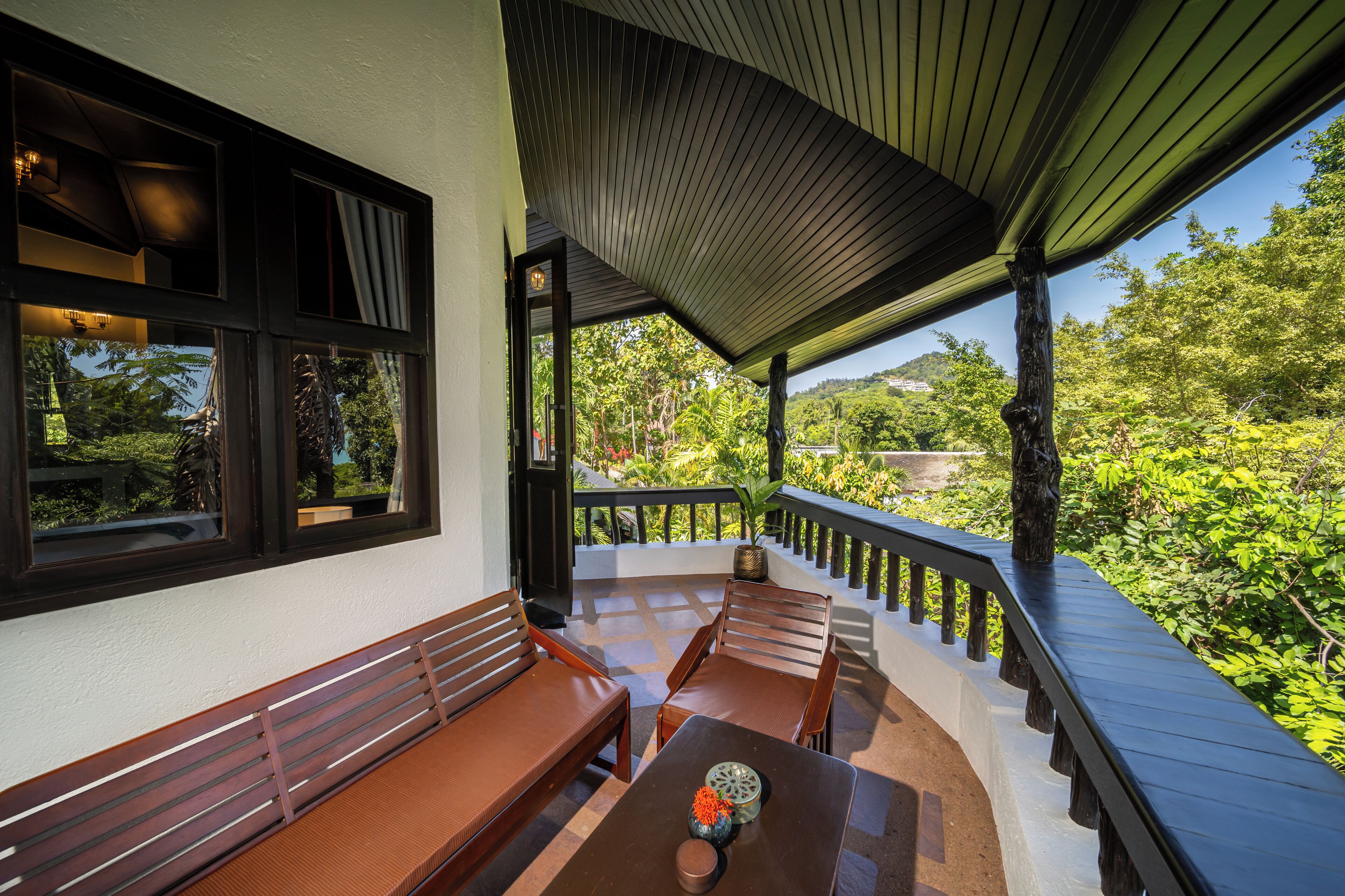 A covered outdoor seating area with wooden benches and a table, surrounded by lush greenery and a view of the landscape.