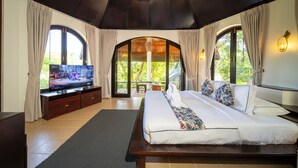 Quarto com uma cama grande, televisão e vista para o verde pelas janelas.