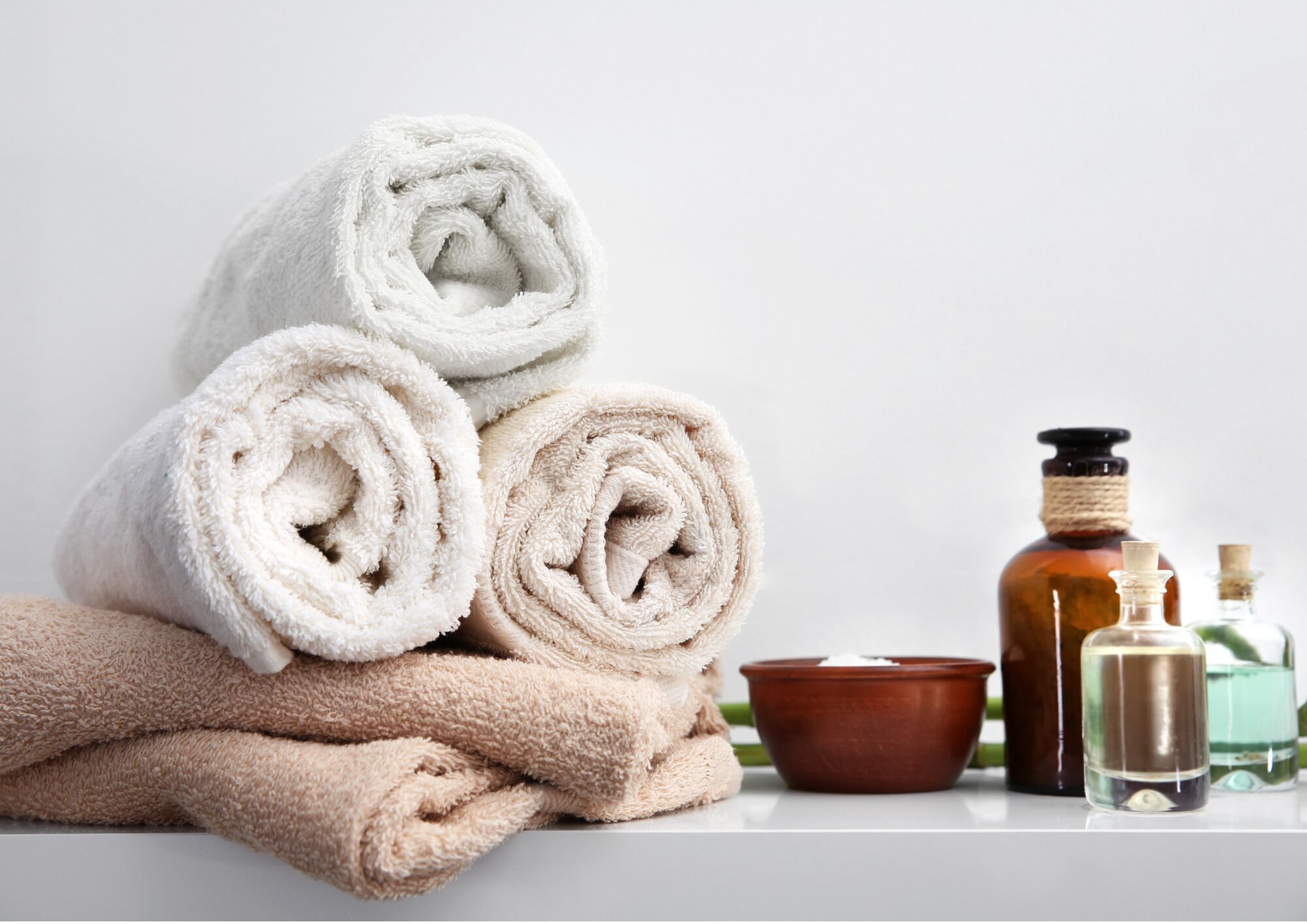 A stack of rolled towels and a few toiletry bottles on a white surface.