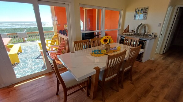 A dining area with a table set for four, a view of the ocean through large windows, and a kitchen area with a sink and stove. - Butiful Beach front House (Bay City)
