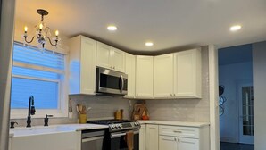 A modern kitchen with white cabinets, a stainless steel microwave, and a herringbone wood floor. - Bright & Spacious Home close to NYC and World Cup (Bayonne)