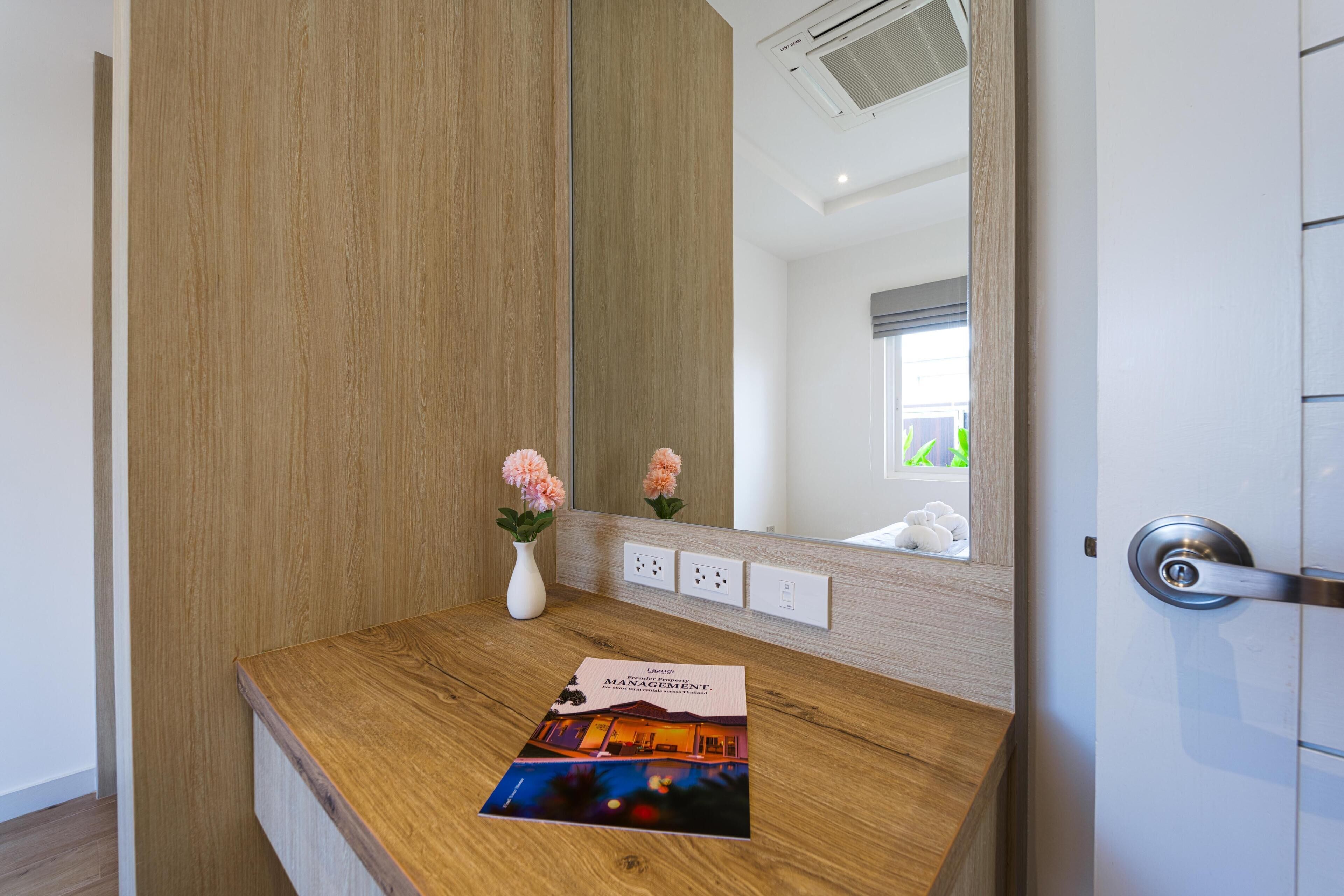 Habitación de hotel con tocador de madera, un espejo, un jarrón con flores y un folleto en la encimera.