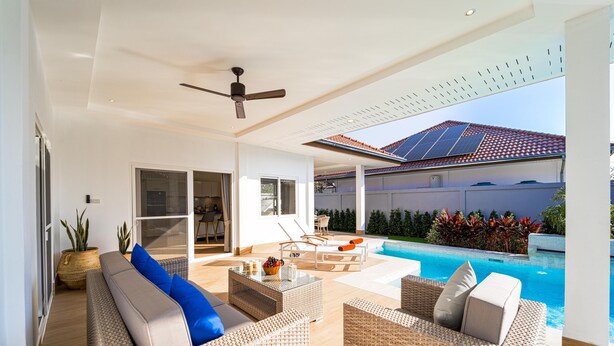 Ein moderner Außenbereich mit Korbmöbeln, Deckenventilator und Pool.