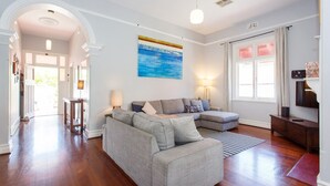 A spacious living room with a sectional sofa, a large painting, and a view of the outdoors through a sliding glass door. - Sunset Views walking distance to Fremantle (Fremantle)