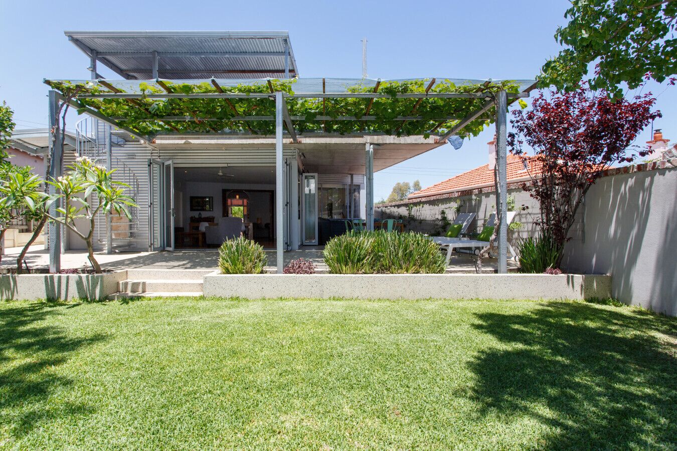 Ein modernes Haus mit überdachter Terrasse, Rasenfläche und Garten.