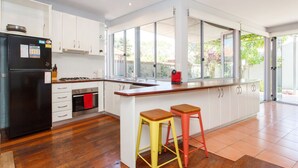A modern kitchen with white cabinets, a black refrigerator, a gas stove, and a large window providing a view of the outdoors. - Sunset Views walking distance to Fremantle (Fremantle)