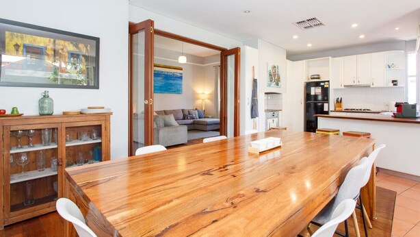 A modern kitchen with white cabinets, a black refrigerator, and a wooden dining table with chairs. - Sunset Views walking distance to Fremantle (Fremantle)