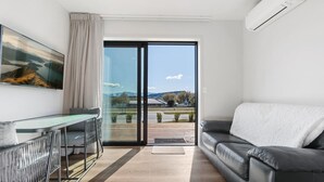 Ein modernes Wohnzimmer mit einem schwarzen Ledersofa, einem Glastisch und einem großen Fenster mit Blick auf eine gebirgige Landschaft.