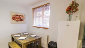 A compact kitchen with a wooden table set for four, a white refrigerator, and a window with blinds. - Leamington Spa House with 4 Bedrooms (Leamington Spa)