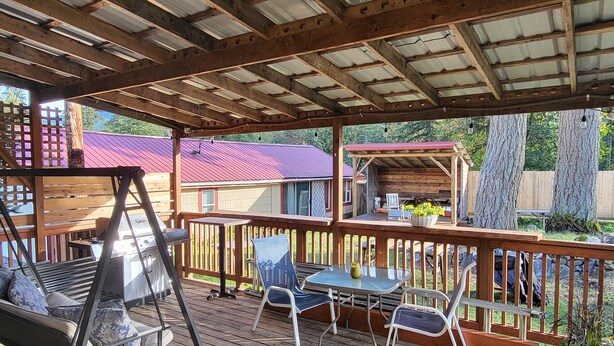 Um deck coberto com churrasqueira, área de estar externa e vista para o quintal.