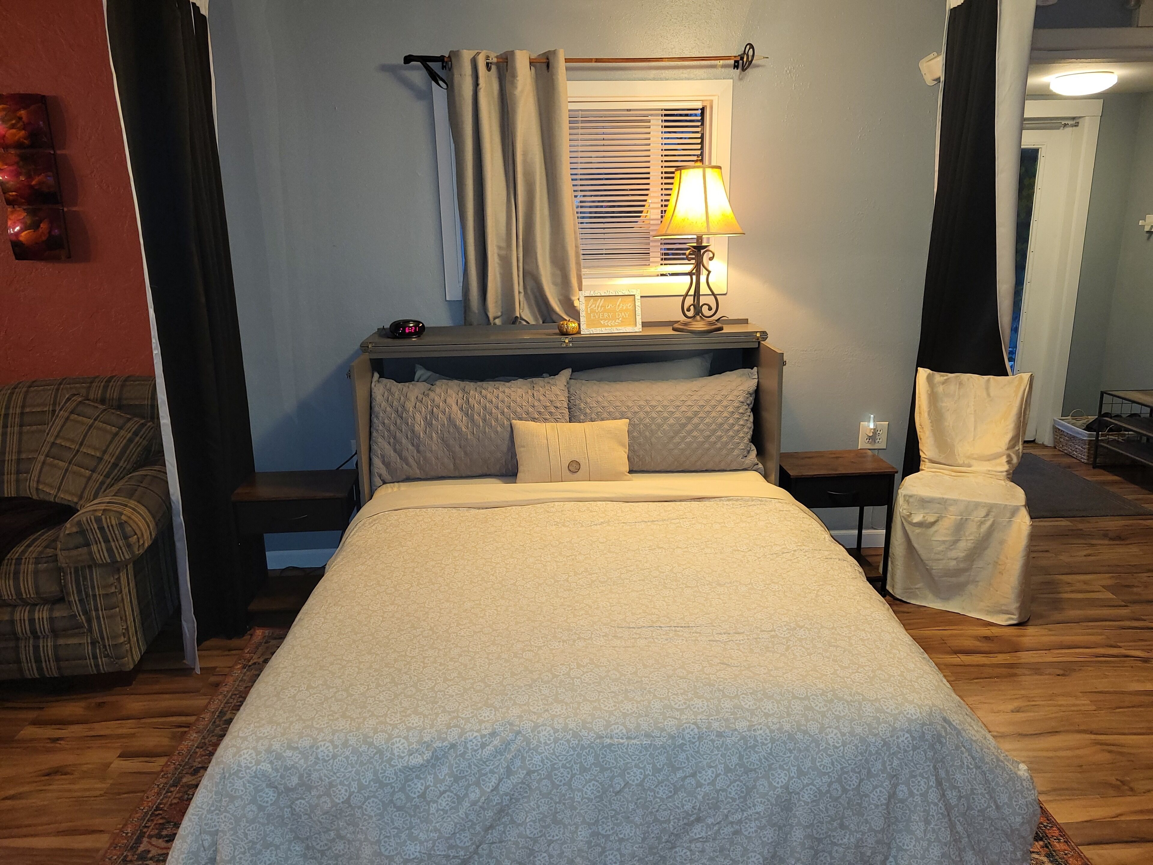 A neatly arranged bedroom with a bed, bedside table, lamp, and a chair.