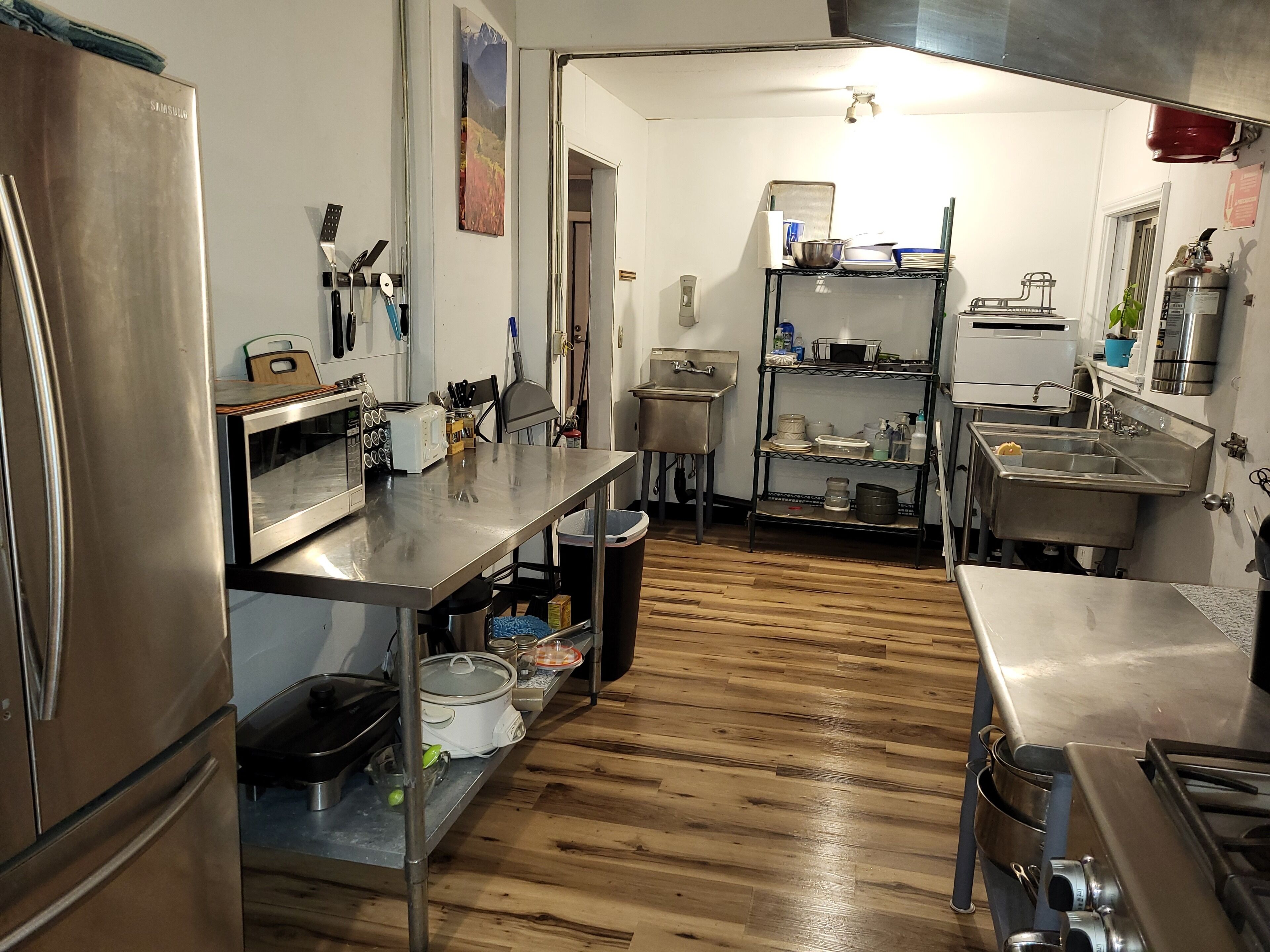 A kitchen with stainless steel appliances, wooden flooring, and a sink area.