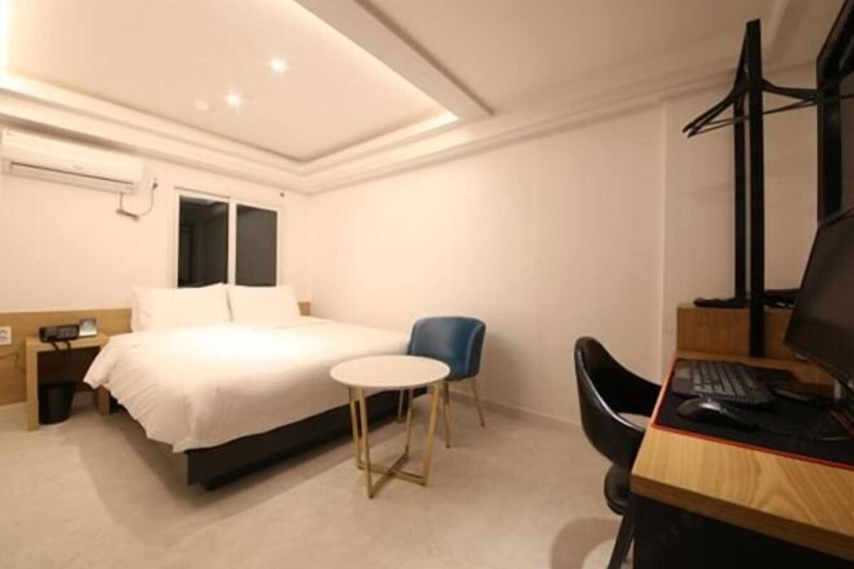 A hotel room with a bed, a desk with a computer, a chair, and a small table.
