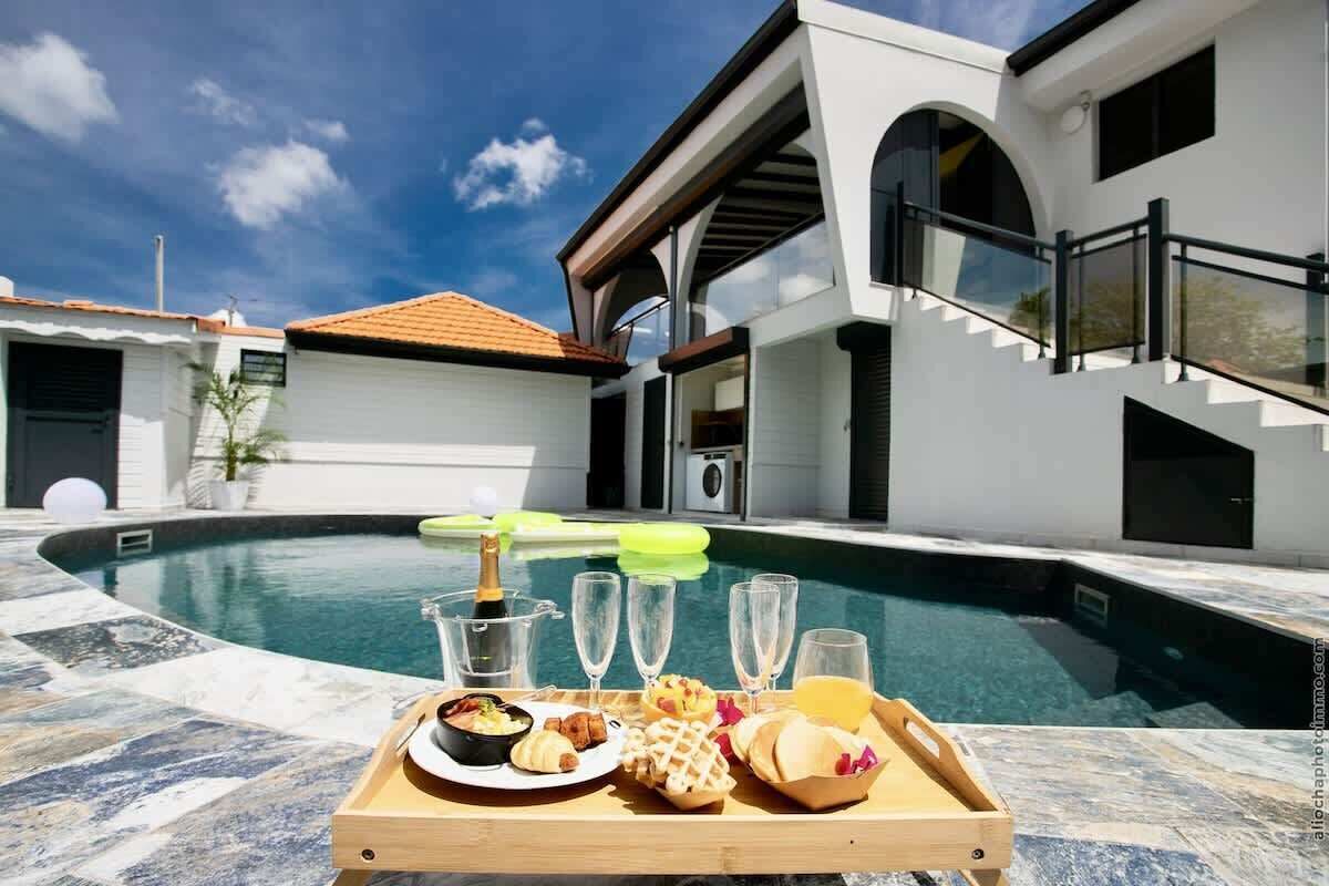 Ein Essbereich am Pool mit einer Serviertablett voller Speisen und Getränke, einer Champagnerflasche und blauem Himmel.