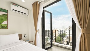 Une chambre d’hôtel équipée d’un lit, d’un climatiseur, d’une table de chevet avec un téléphone et offrant une vue sur la ville depuis une porte-fenêtre donnant sur un balcon.