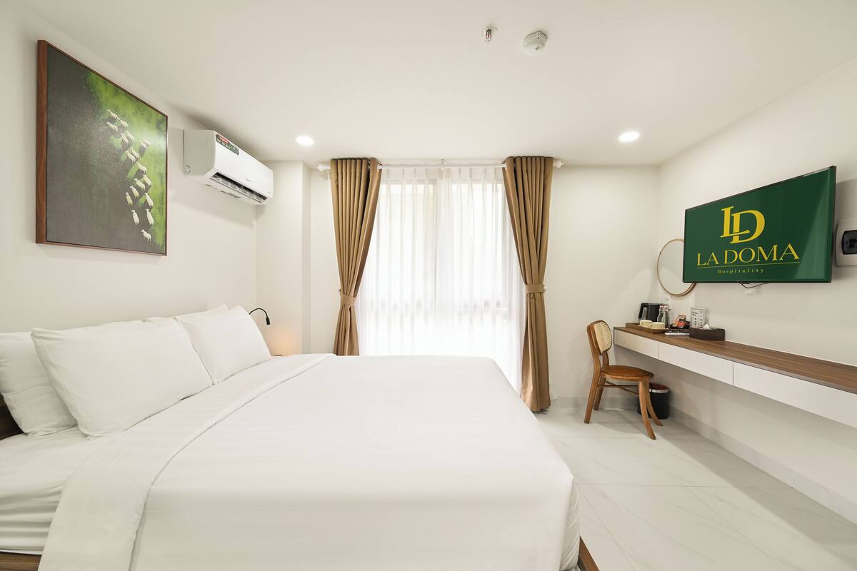 Habitación de hotel con cama, escritorio, silla, televisión y ventana con cortinas.
