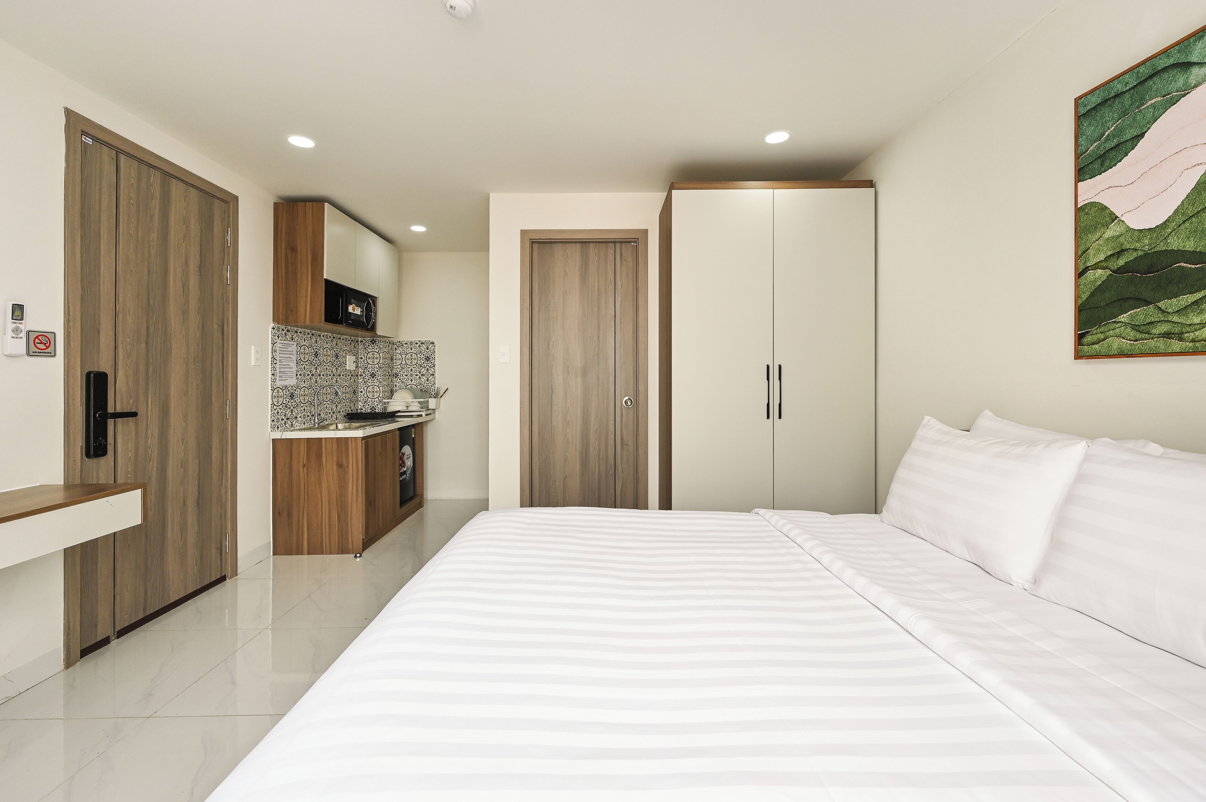 A modern bedroom with a large bed, a wardrobe, and a kitchenette area.