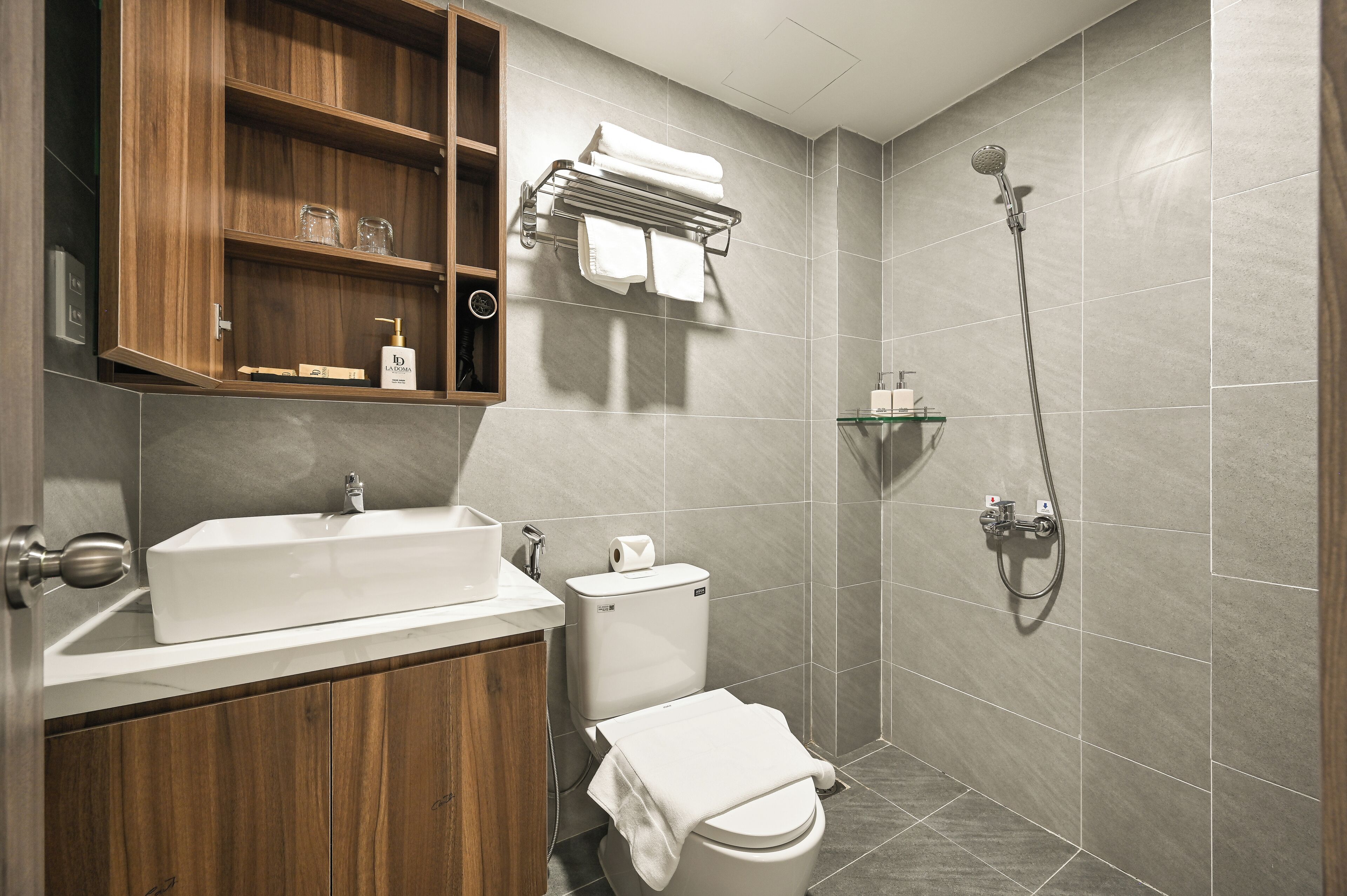 A modern bathroom with a wooden vanity, a white sink, a toilet, and a shower area.