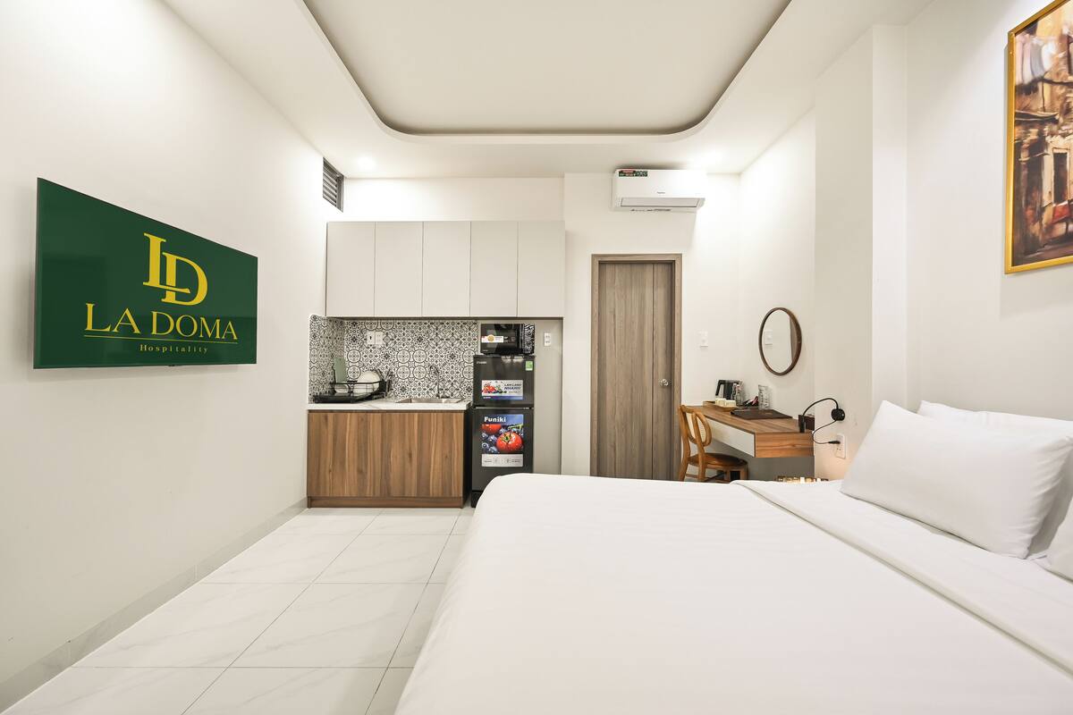 Habitación de hotel con cama, escritorio, kitchenette y puerta.