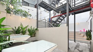 Une cour intérieure avec une table en verre, des plantes en pot et un escalier.