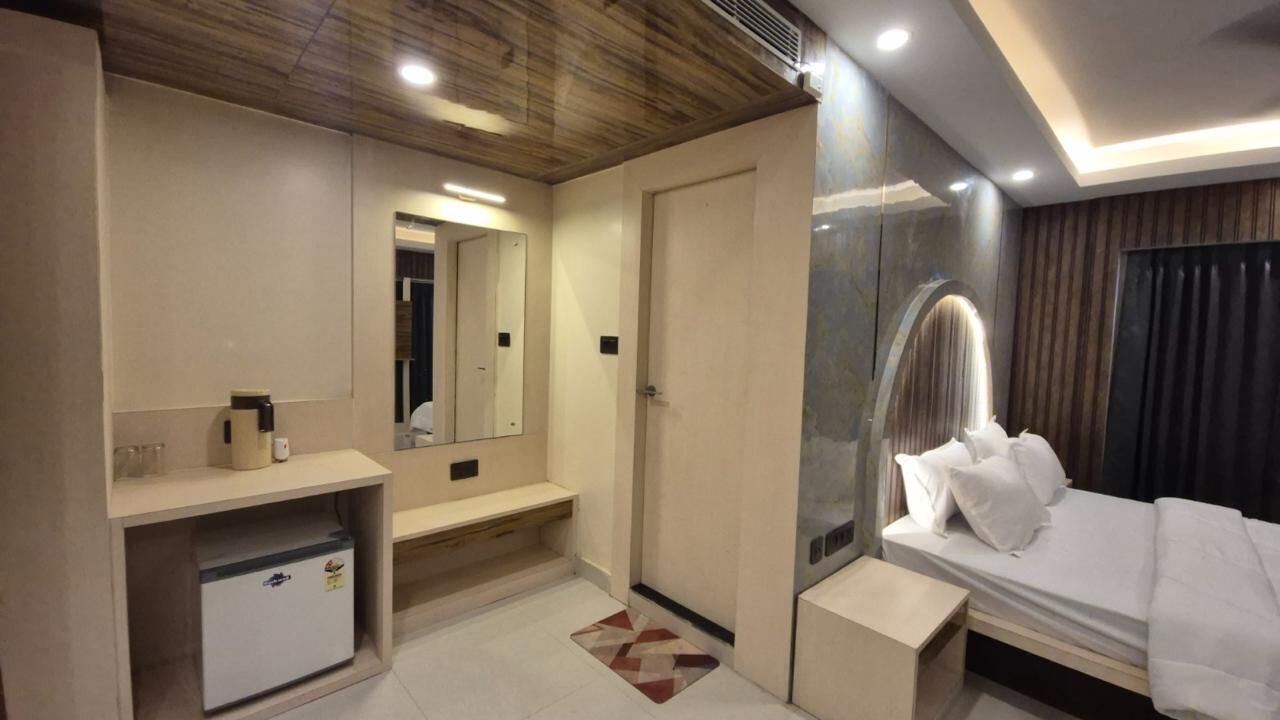 Una habitación de hotel moderna con cama, mesita de noche, espejo y una pequeña zona de estar.