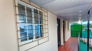 A corridor with a tiled floor, a window with a metal grid, and a green fence outside.