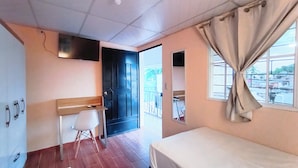 A hotel room with a bed, a desk, a chair, a TV mounted on the wall, and a window with curtains.