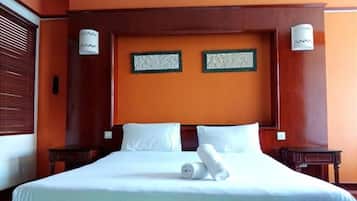 Hotellihuone, jossa on suuri sänky, kaksi seinään kiinnitettyä lamppua ja puinen pääty.