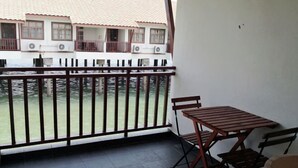 A balcony with a view of a building across the water, a table with chairs, and a railing. - Premium Water Chalet 2 (Port Dickson)
