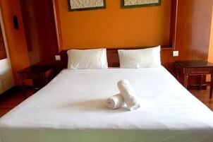 Una cama bien hecha con sábanas blancas y dos toallas enrolladas, mesitas de noche de madera y un cabecero de madera.