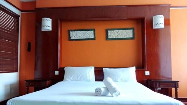 A hotel room with a large bed, two wall-mounted lamps, and a wooden headboard. - Premium Water Chalet 2 (Port Dickson)
