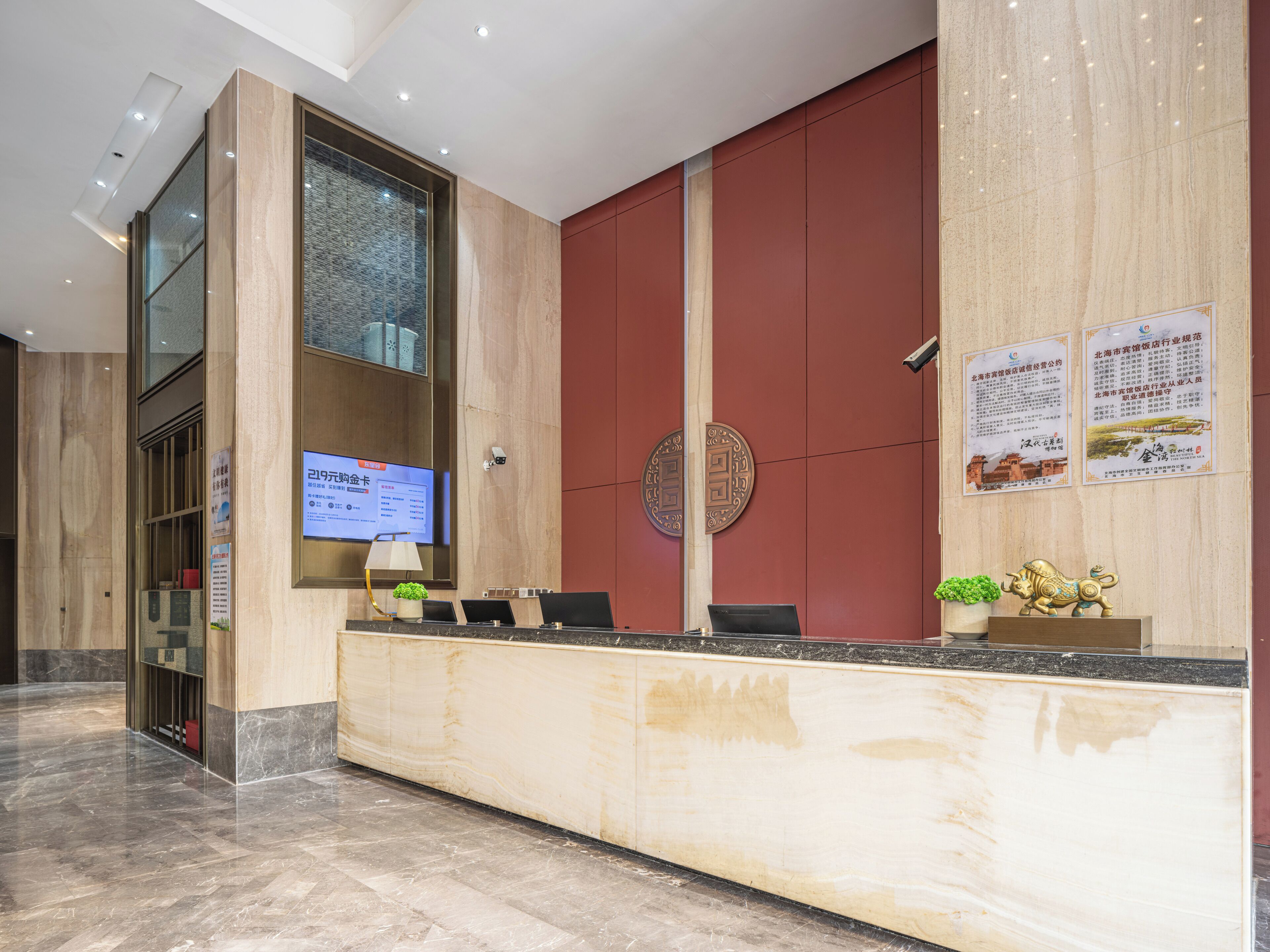 A hotel reception area with a marble reception desk, a digital screen displaying information, and a large red wall with decorative elements.