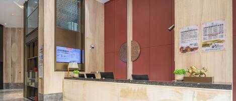 A hotel reception area with a marble reception desk, a digital screen displaying information, and a large red wall with decorative elements.