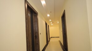 A hallway with wooden doors, each marked with a number. The floor is tiled with a marble pattern. - HOTEL CRESTA INN (Agra)