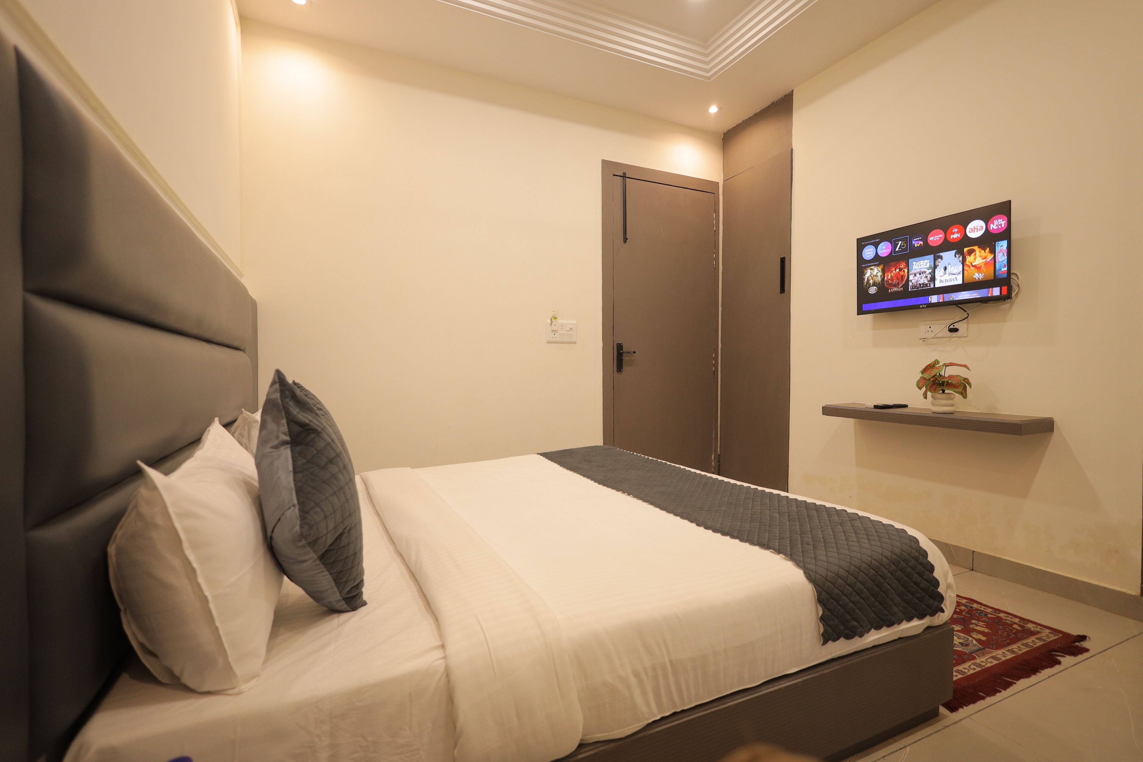 Une chambre moderne avec un lit, des oreillers, une télévision et une petite étagère.