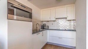 Eine kleine Küche mit weißen Schränken, einem Edelstahlbackofen, einer Spüle und einer Kaffeemaschine.