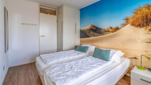 Ein Schlafzimmer mit zwei Betten, einem Kleiderschrank und einem Wandbild mit Wüstenthema.