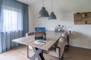 Uma área de refeições com mesa de madeira, cadeiras bege e duas luminárias pendentes.