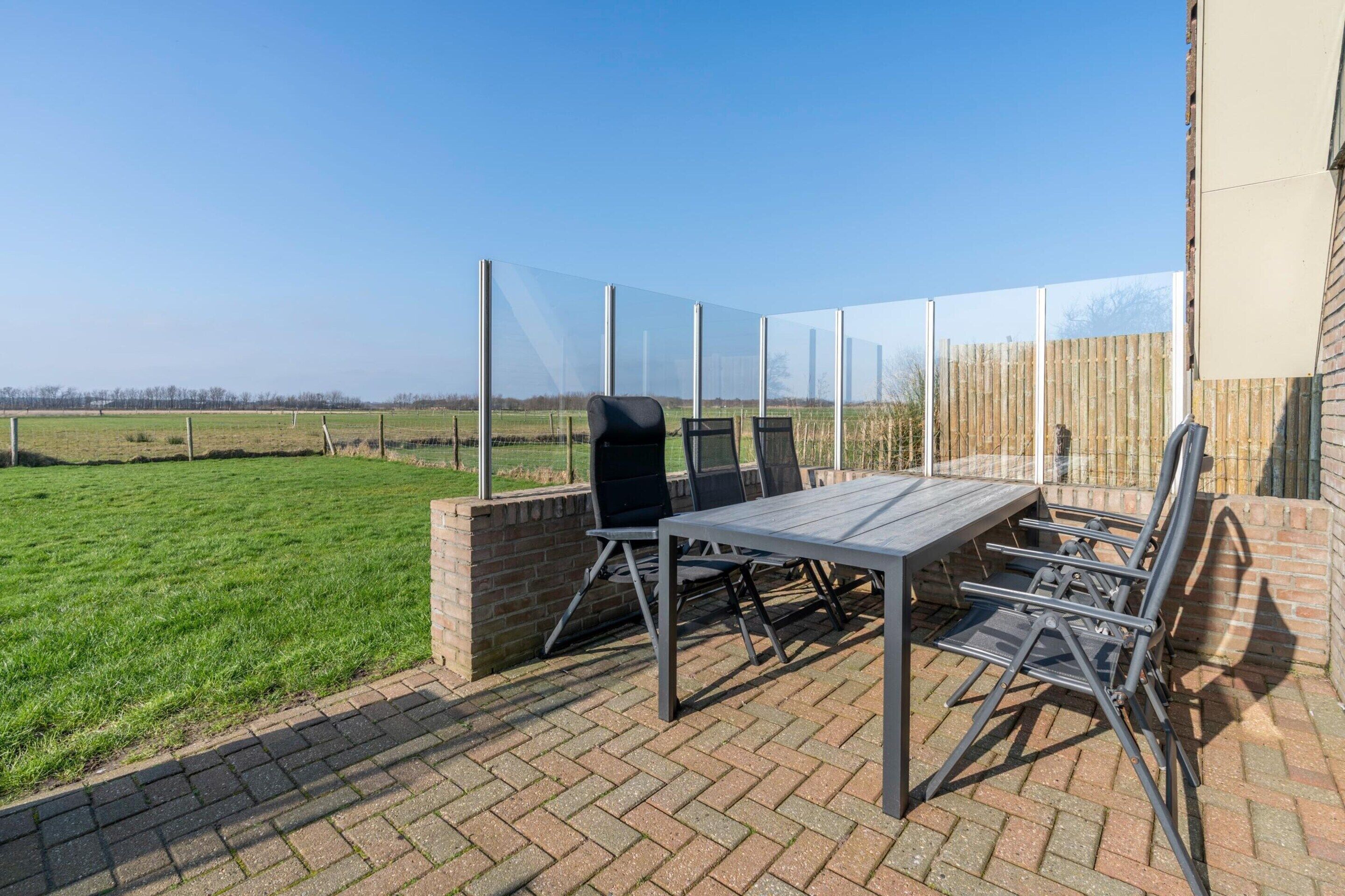 An outdoor patio with a table and chairs, a brick wall, and a view of a field.