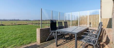 An outdoor patio with a table and chairs, a brick wall, and a view of a field.