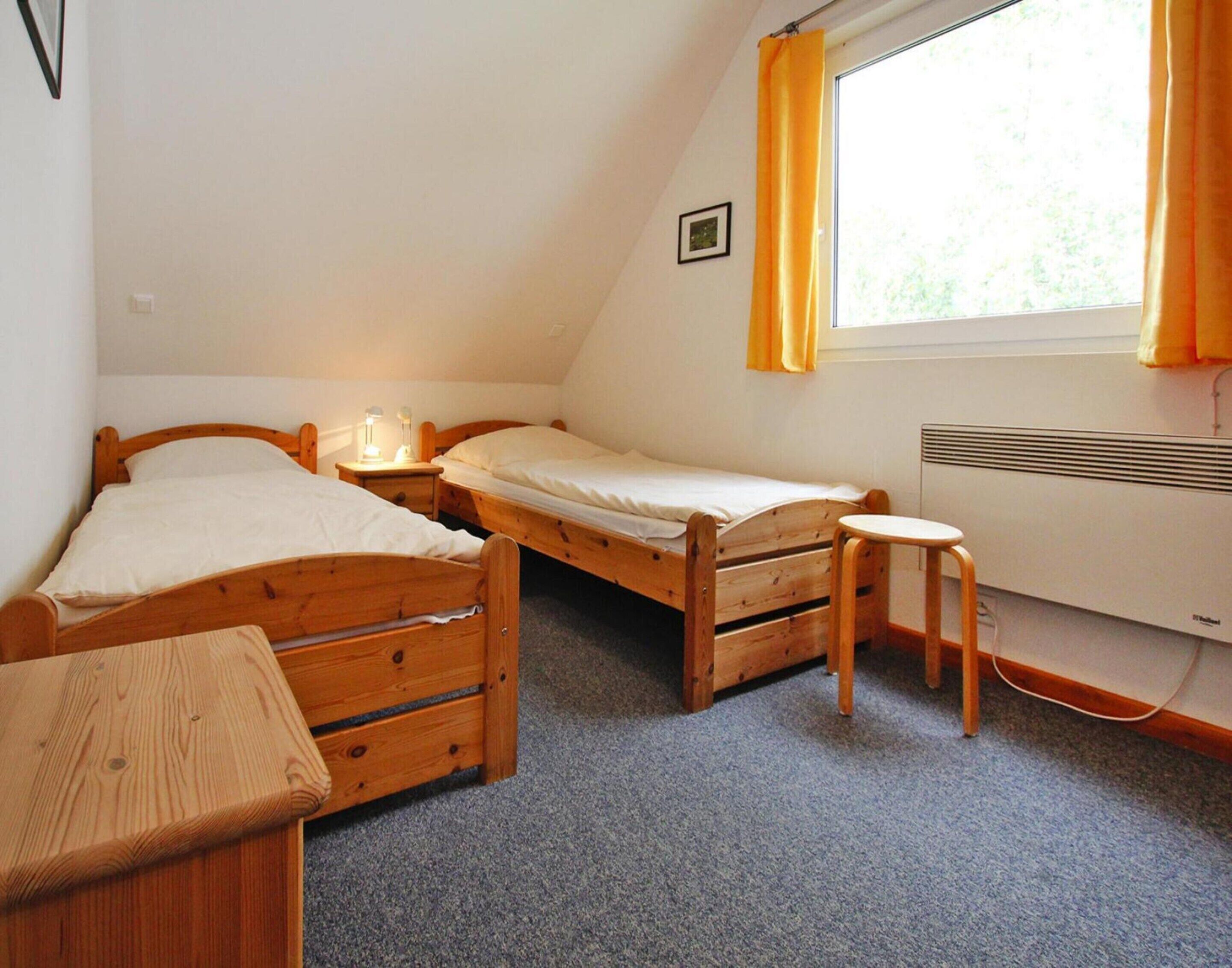 Una habitación pequeña y acogedora con dos camas de madera, una mesita y una ventana con cortinas.