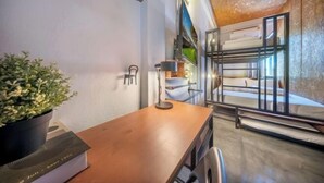 A room with a wooden desk, a potted plant, a lamp, bunk beds, and a view of the outdoors. - Ralph Bangkok (Bangkok)