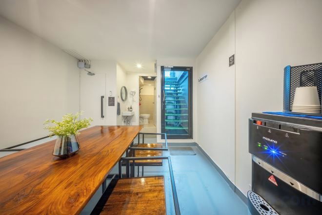 A modern kitchen with a wooden table, a coffee machine, and a staircase leading to an upper floor.